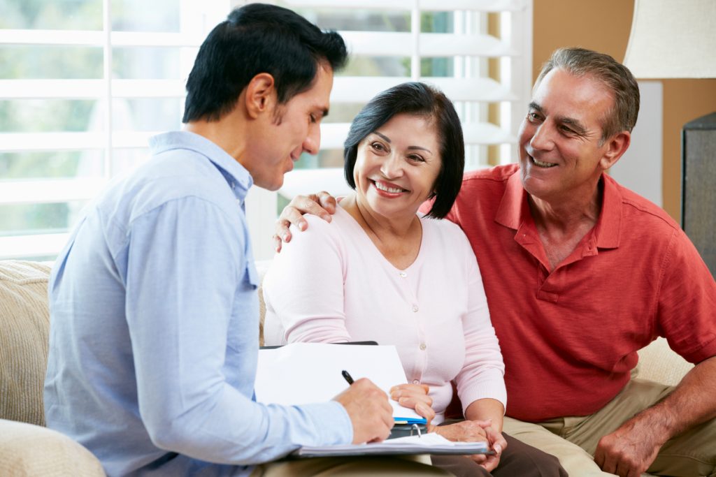 Financial Advisor Talking To Senior Couple At Home Writing Documents Smiling. Concept: Business Loan Fees