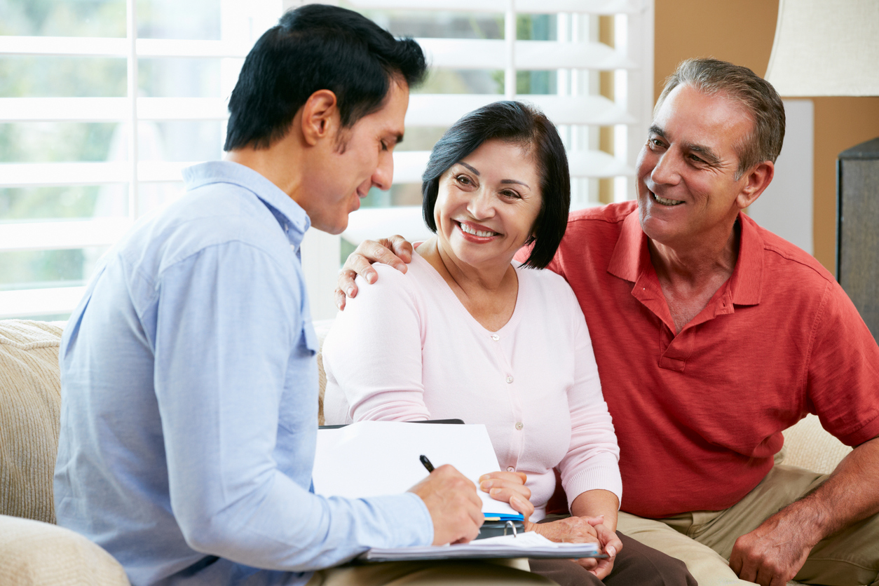 Financial Advisor Talking To Senior Couple At Home Writing Documents Smiling. Concept: Business Loan Fees