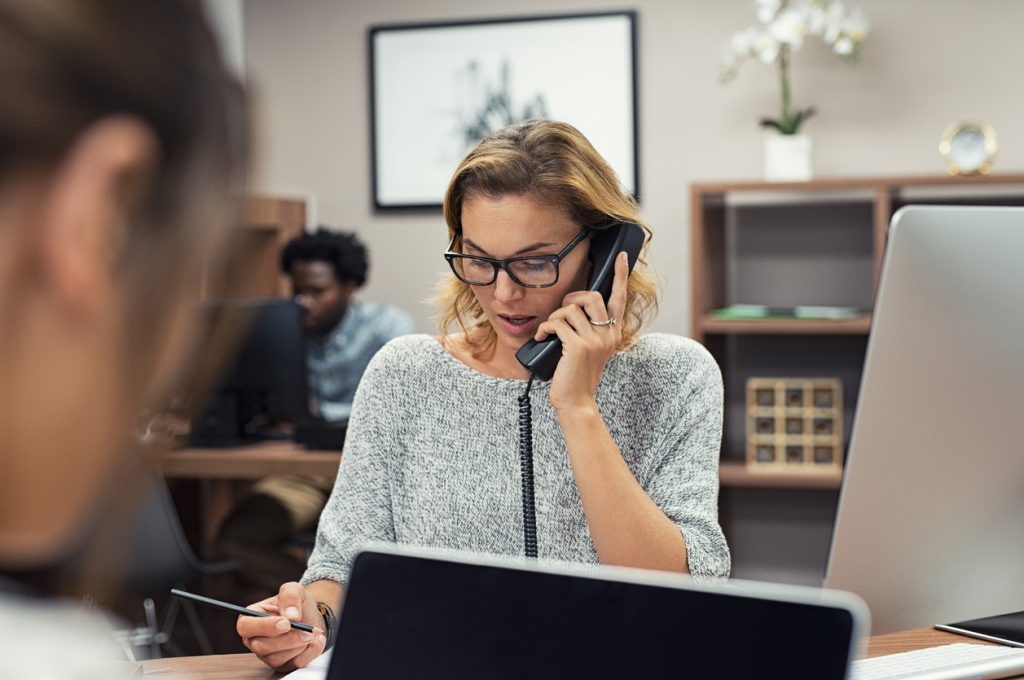 Empleada hablando por teléfono fijo en oficina. Concepto: Planes de telefonía fijos o planes de telefonía móvil