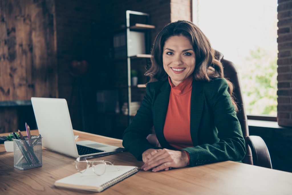 Foto de una empresaria sentada en su oficina trabajando frente a un cuaderno y una laptop. Concept: software de impuestos