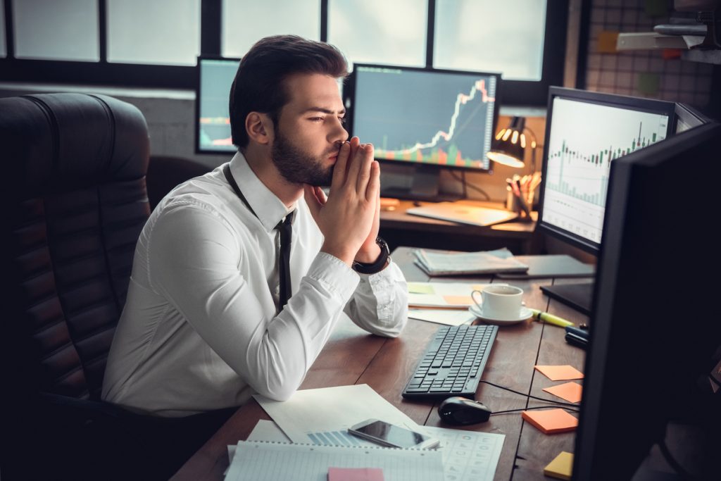 Man trader at office sitting at table looking at monitors wondering options vs stocks?