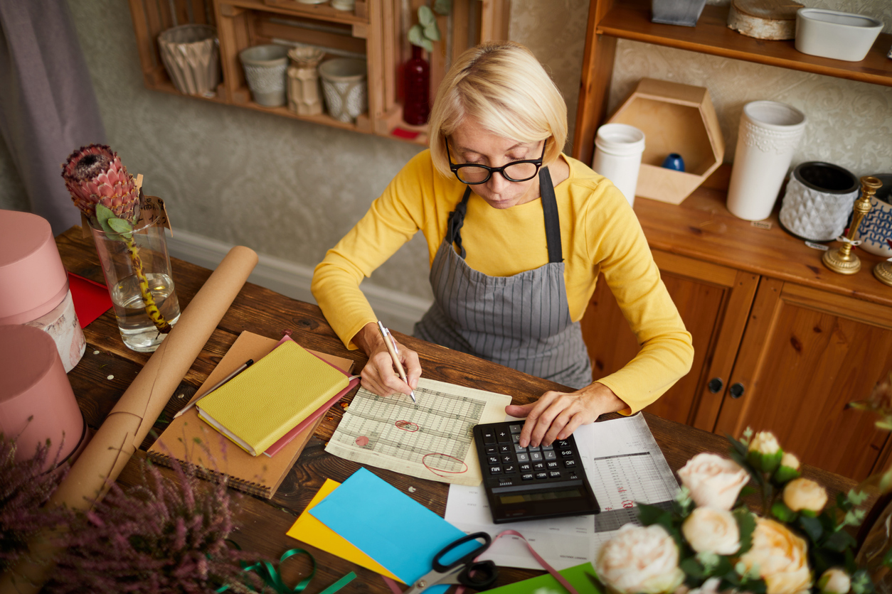 High angle portrait of female businesswoman counting finances using calculator in small shop, copy space. Concept: quarterly taxes