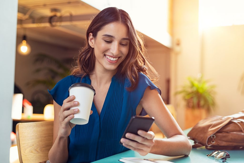 Mujer joven sosteniendo su café mientras mira su celular, llamada de negocios. concept: mejores planes celulares