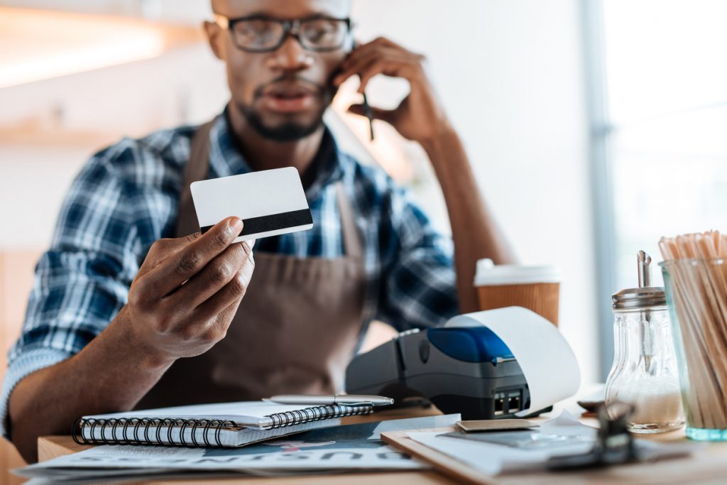 Coffee shop owner working with credit card reader and smartphone in coffee shop. Concept: secured credit card.