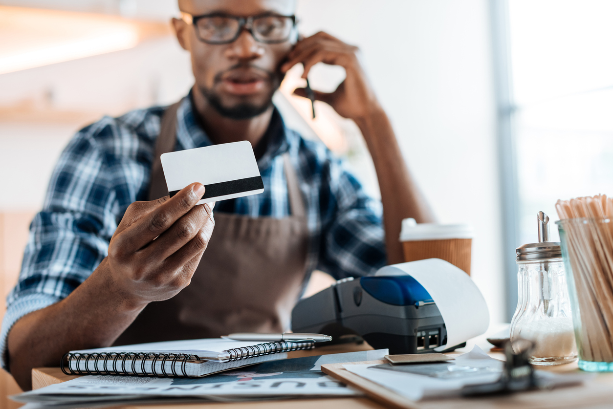 Coffee shop owner working with credit card reader and smartphone in coffee shop. Concept: secured credit card.