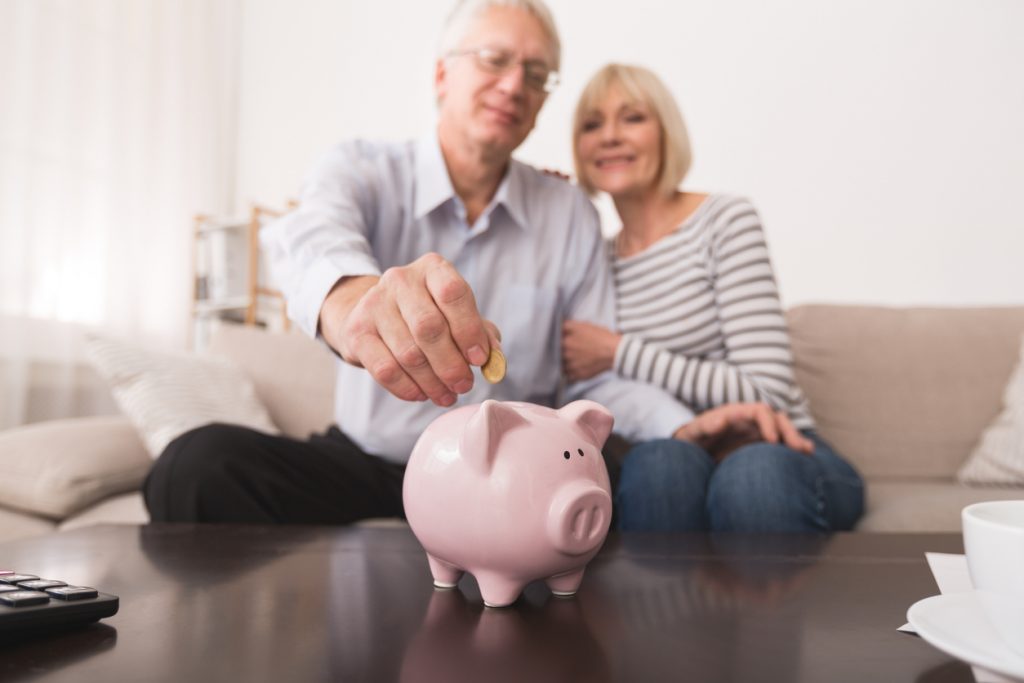 Senior couple putting coin in piggybank, saving money at home. Concept: What are annuities?