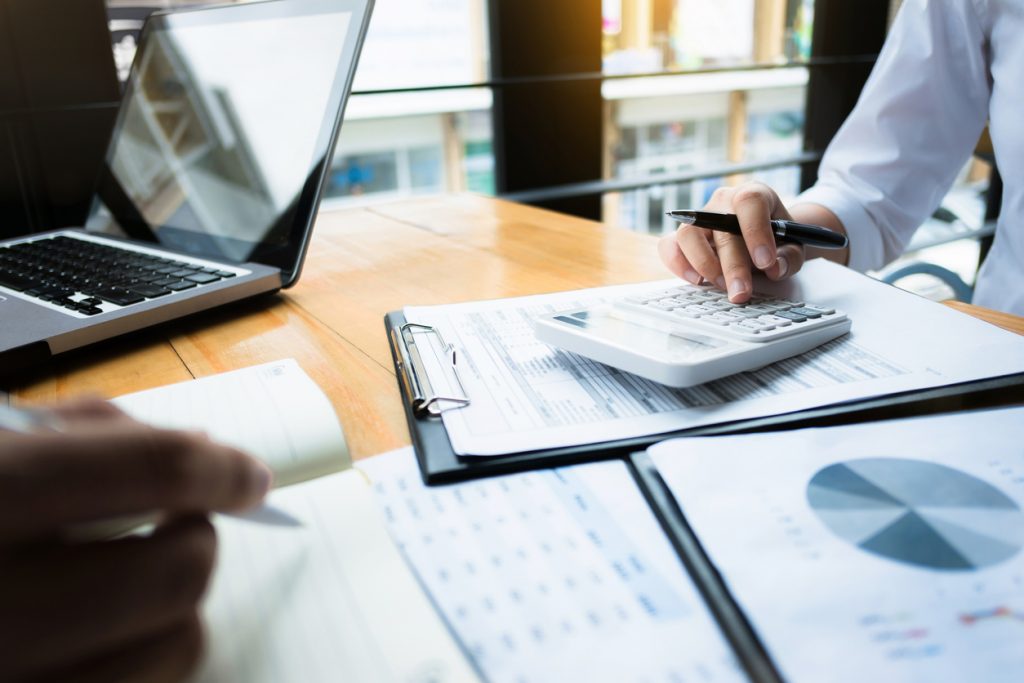 Auditoría en un negocio, personas usando calculadora, datos financieros, inversiones. Concept: seguimiento de gastos comerciales