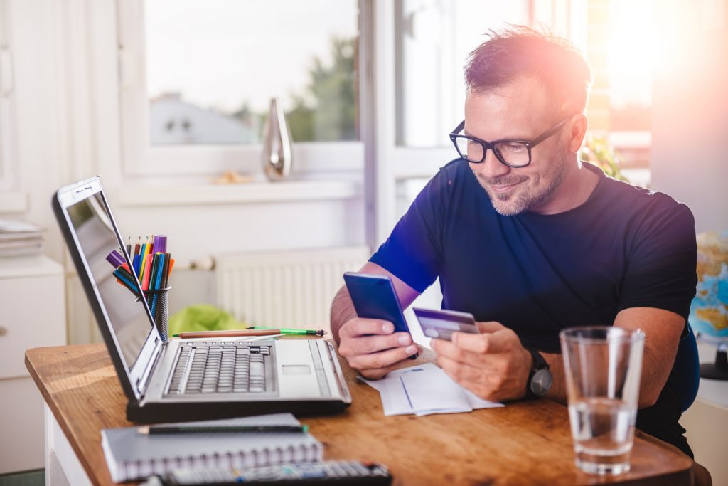 Man paying with credit card on smart phone at home office. Concept: how to choose a credit card