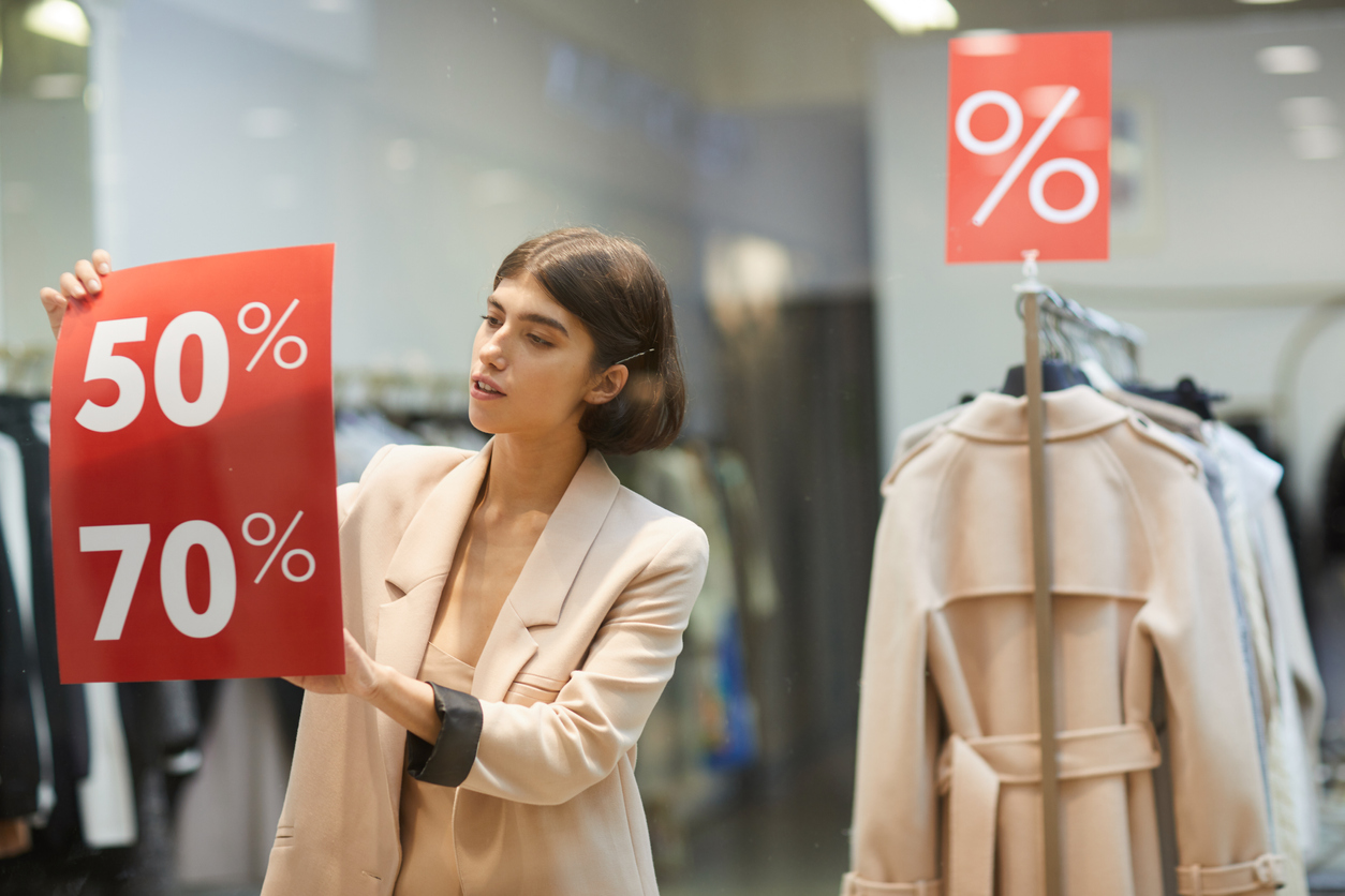 Waist up portrait of beautiful woman hanging red SALE signs on window display in clothes store, copy space. Concept: black friday tips
