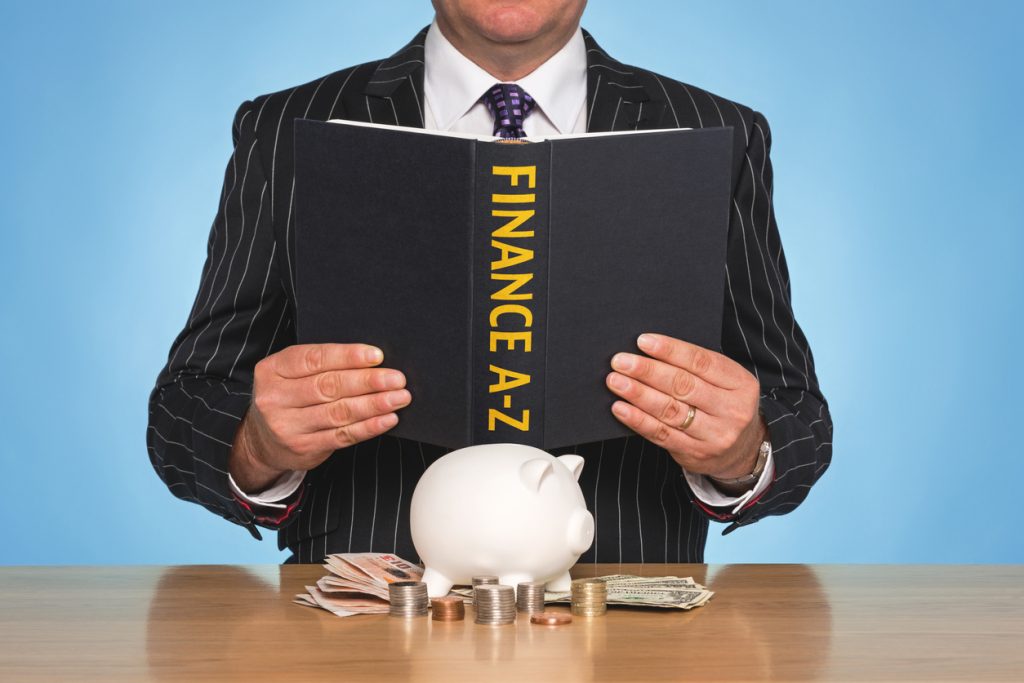 A businessman sat at a desk reading a FINANCE A-Z book. Concept: financial terms
