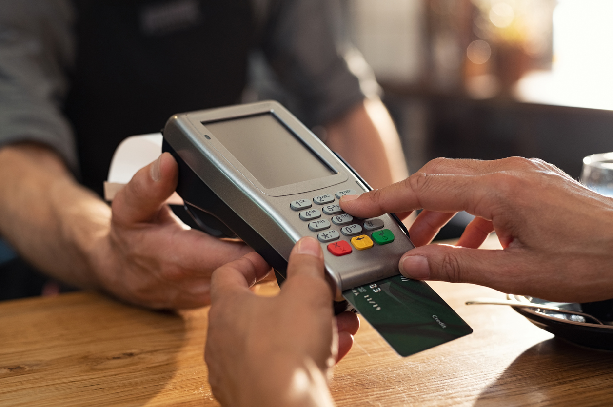 Closeup of hand using credit card swiping machine to pay. Female hand with credit card paying through terminal for payment in coffee shop. Woman entering debit card code in swipe machine. Concept: credit utilization