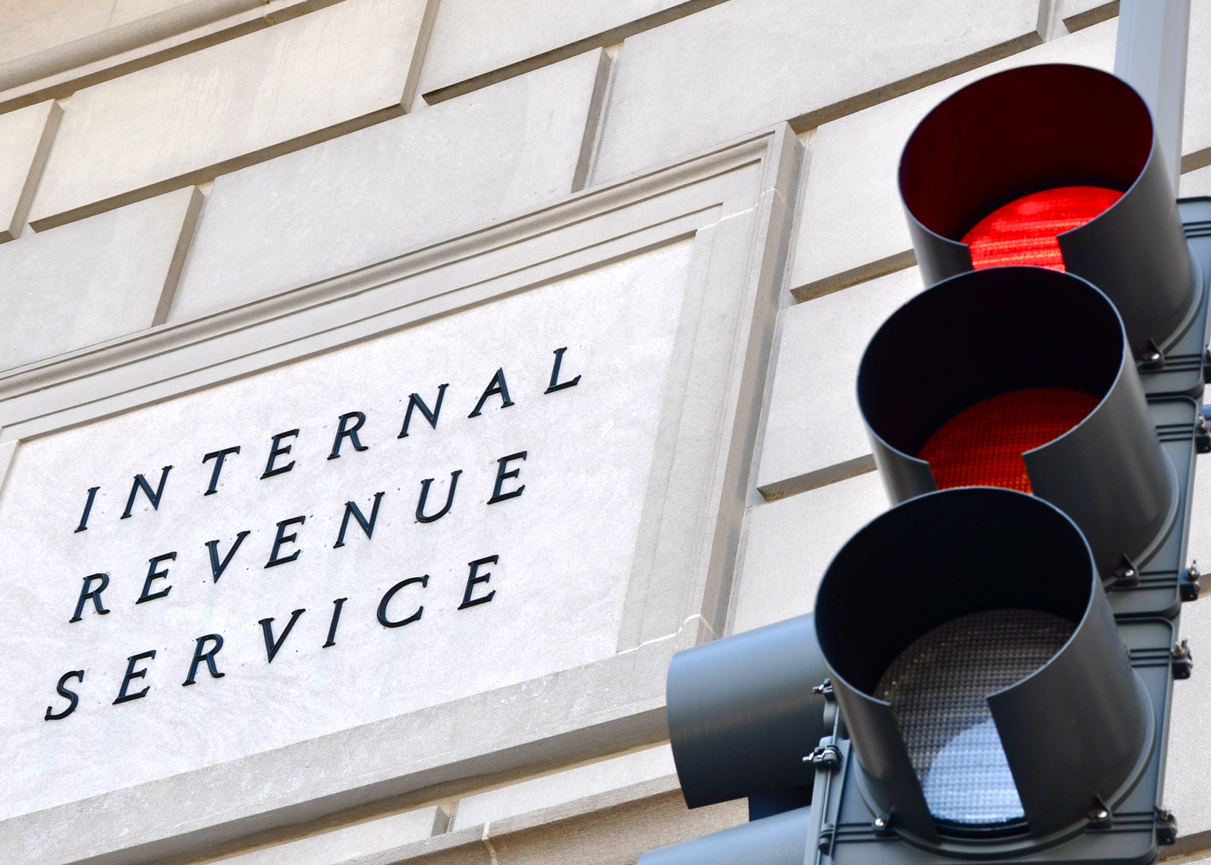 Internal Revenue Service sign with a traffic signal in the foreground indicating a red light. concept: back taxes