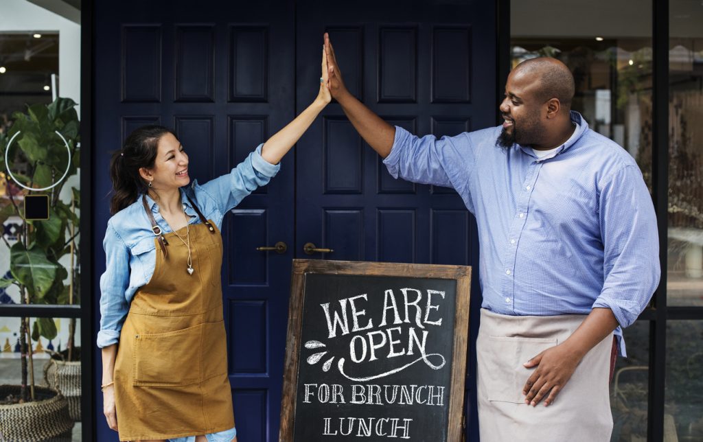 Dueños de una asociación comercial celebrando apertura a la puerta de su restaurante