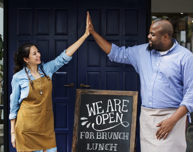 Dueños de una asociación comercial celebrando apertura a la puerta de su restaurante