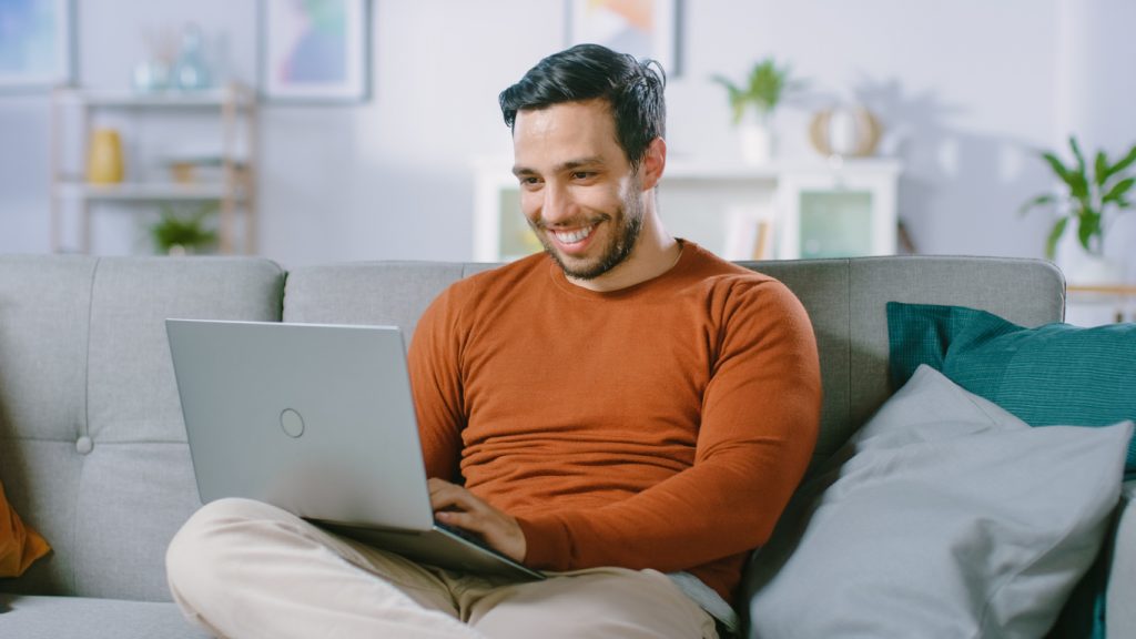 Hombre feliz en un sillón navegando por internet en tu laptop. concept: página web comercial