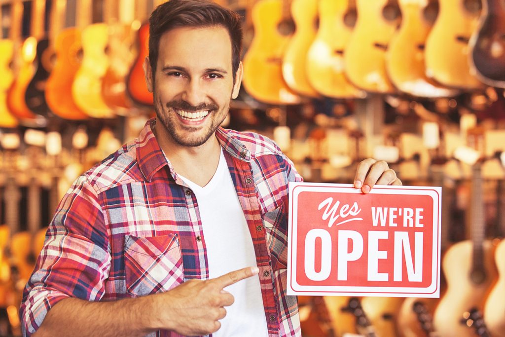 Musical intruments store. Young salesperson is showing open store sign. Concept: going concern assumption