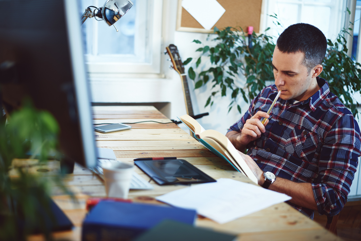 Young man sitting in a home office, reading some book. Concept: marketing books