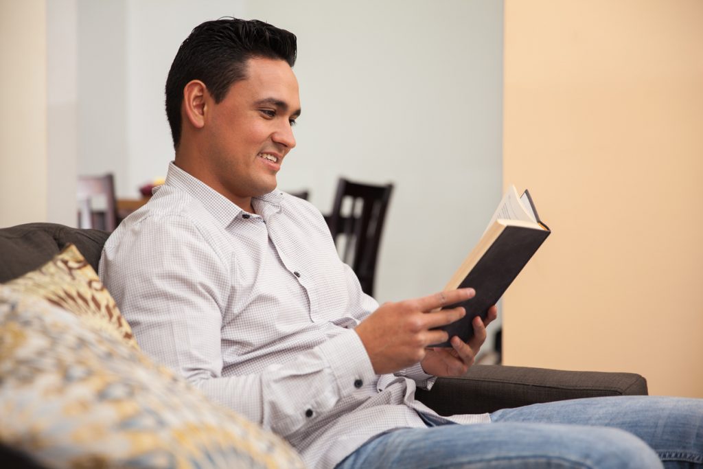 Hombre latino relajándose en casa leyendo un libro. Concept: libros para emprendedores