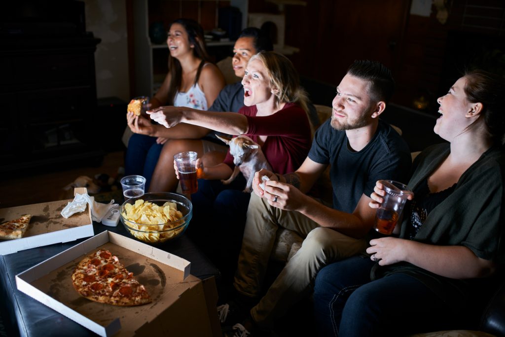 Group of friends watching the best business movies and eating popcorn and pizza.
