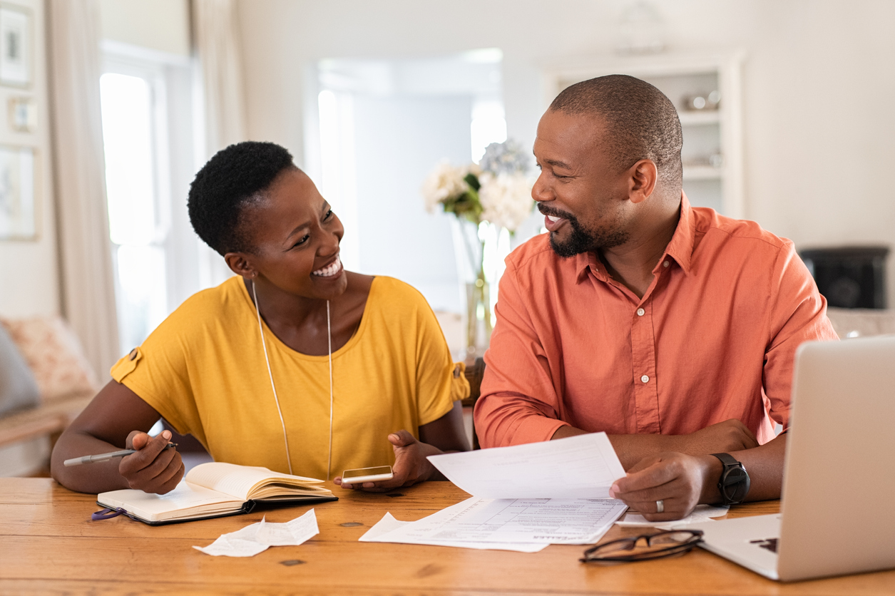 Cheerful mature couple sitting and managing expenses at home. Happy african man and woman paying bills together and managing budget. Black smiling couple checking accountancy and bills while looking at each other. concept: What Is A UCC Filing