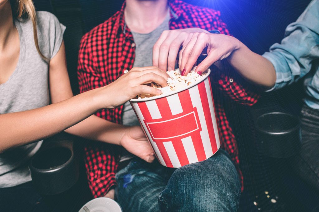 Close up of red with white basket of popcorn that both girl and guy are holding.