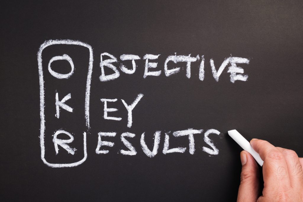 Hand writing text and acronym of OKR (Objective Key Results) on chalkboard. concept: OKR examples