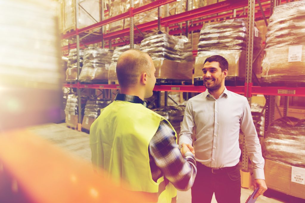 wholesale, logistic, people and export concept - manual worker and businessmen with clipboard shaking hands and making deal at warehouse. concept: trade credit