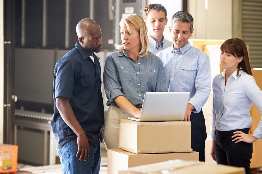 Workers In Warehouse Using Laptop Discussing costs of goods sold.