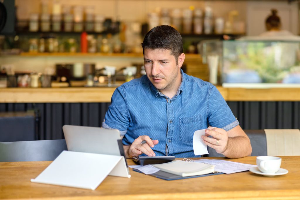 Coffee shop owner with bills, receipys and laptop working on taxes. Concept: Schedule C.