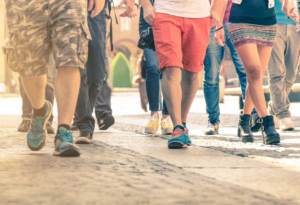 Crowd of people walking on the street - Detail of legs and shoes moving on sidewalk in city center - Travellers with multicolor clothes on vintage filter - Shallow depth of field with sunflare halo. concept: foot traffic