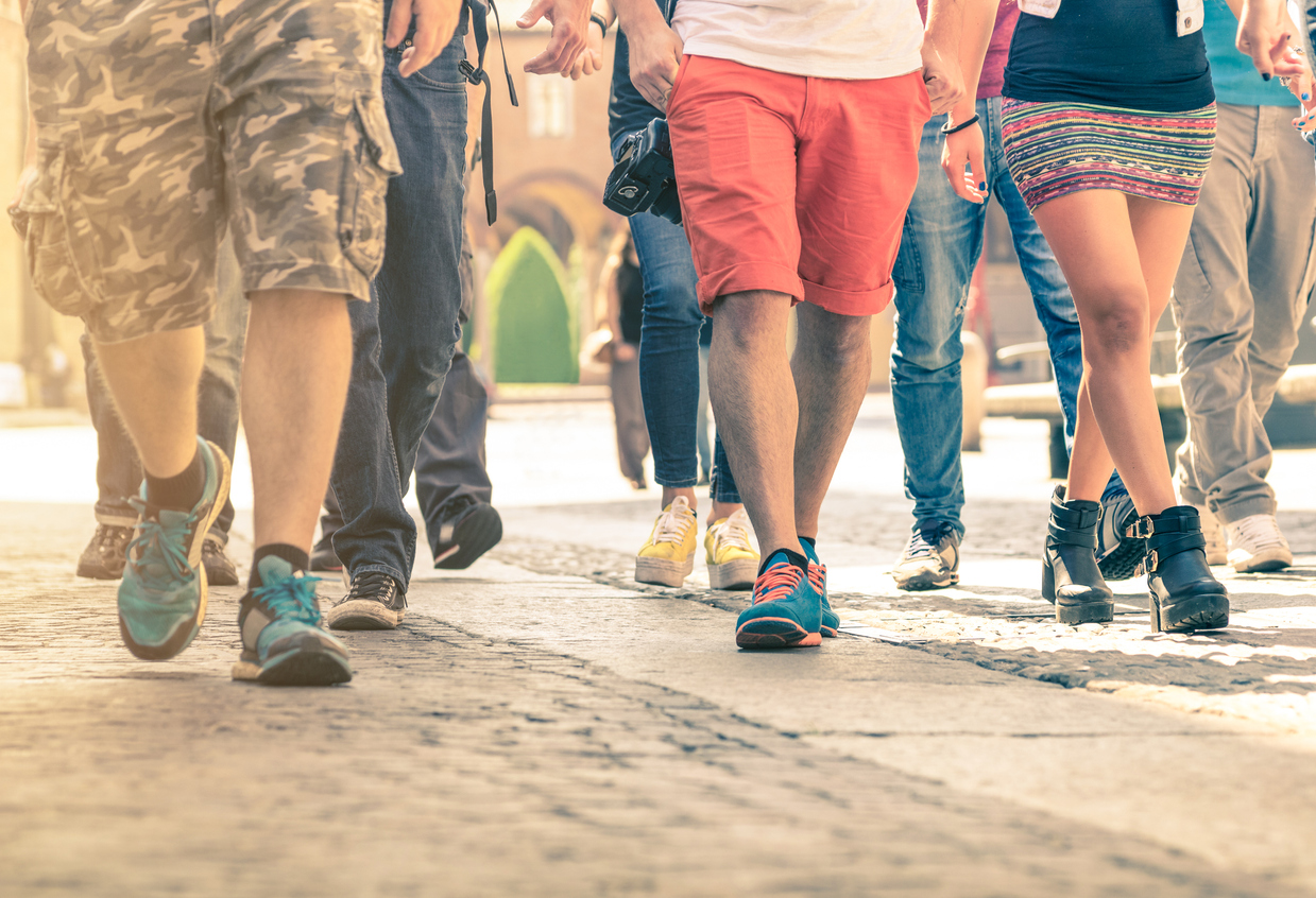 Crowd of people walking on the street - Detail of legs and shoes moving on sidewalk in city center - Travellers with multicolor clothes on vintage filter - Shallow depth of field with sunflare halo. concept: foot traffic