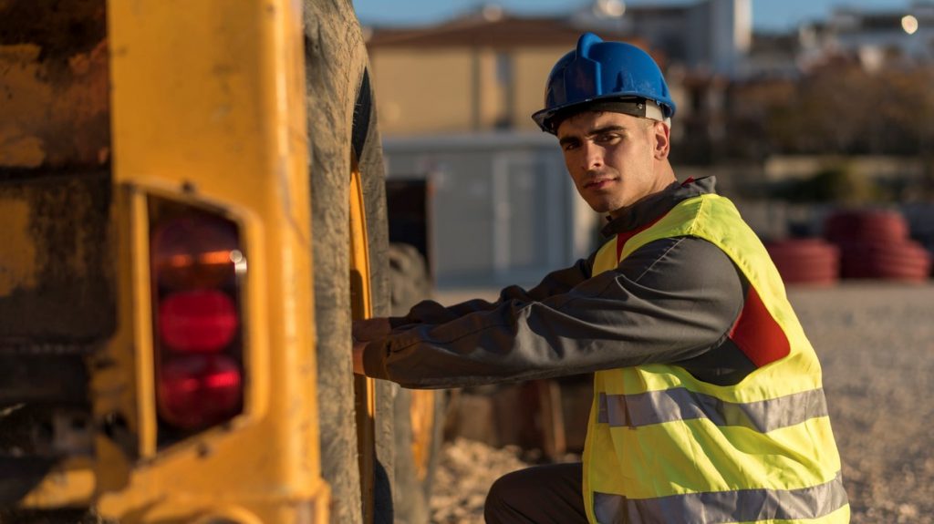 Trabajador en construcción revisando la llanta de la excavadora. concept: maquinaria de construcción