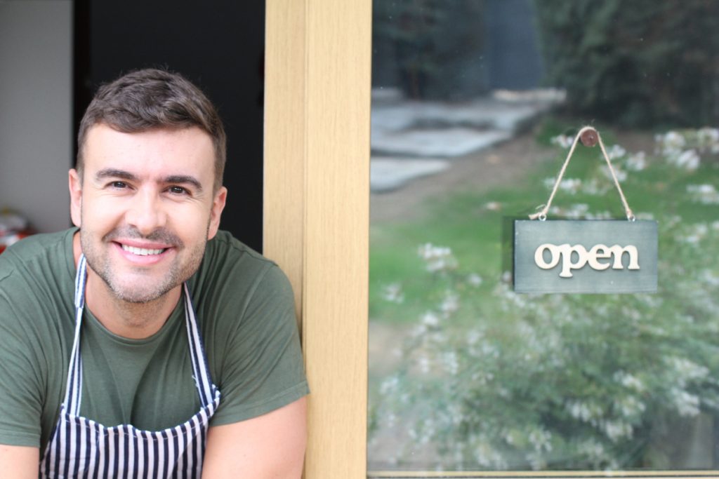 Empresario sonriendo frente a su negocio. concept: razones para obtener un préstamo
